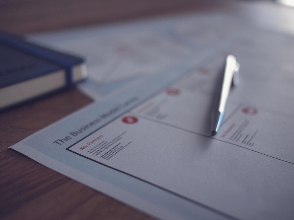 An image show a Business Model Canvas template on a desk with a pen, ready to complete the Business Strategy.